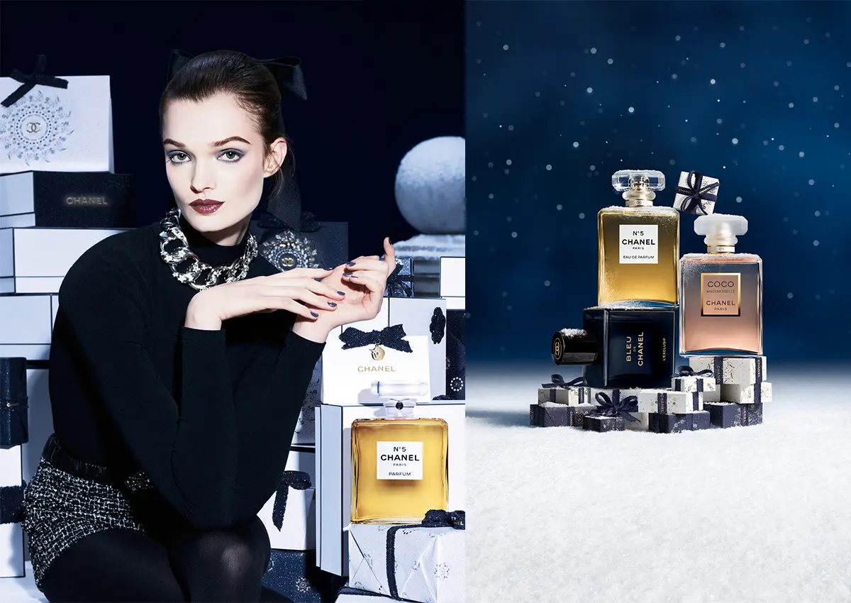 Zimska kolekcija Chanel z ikoničnimi parfumi in prazničnimi darili na temno modrem ozadju.