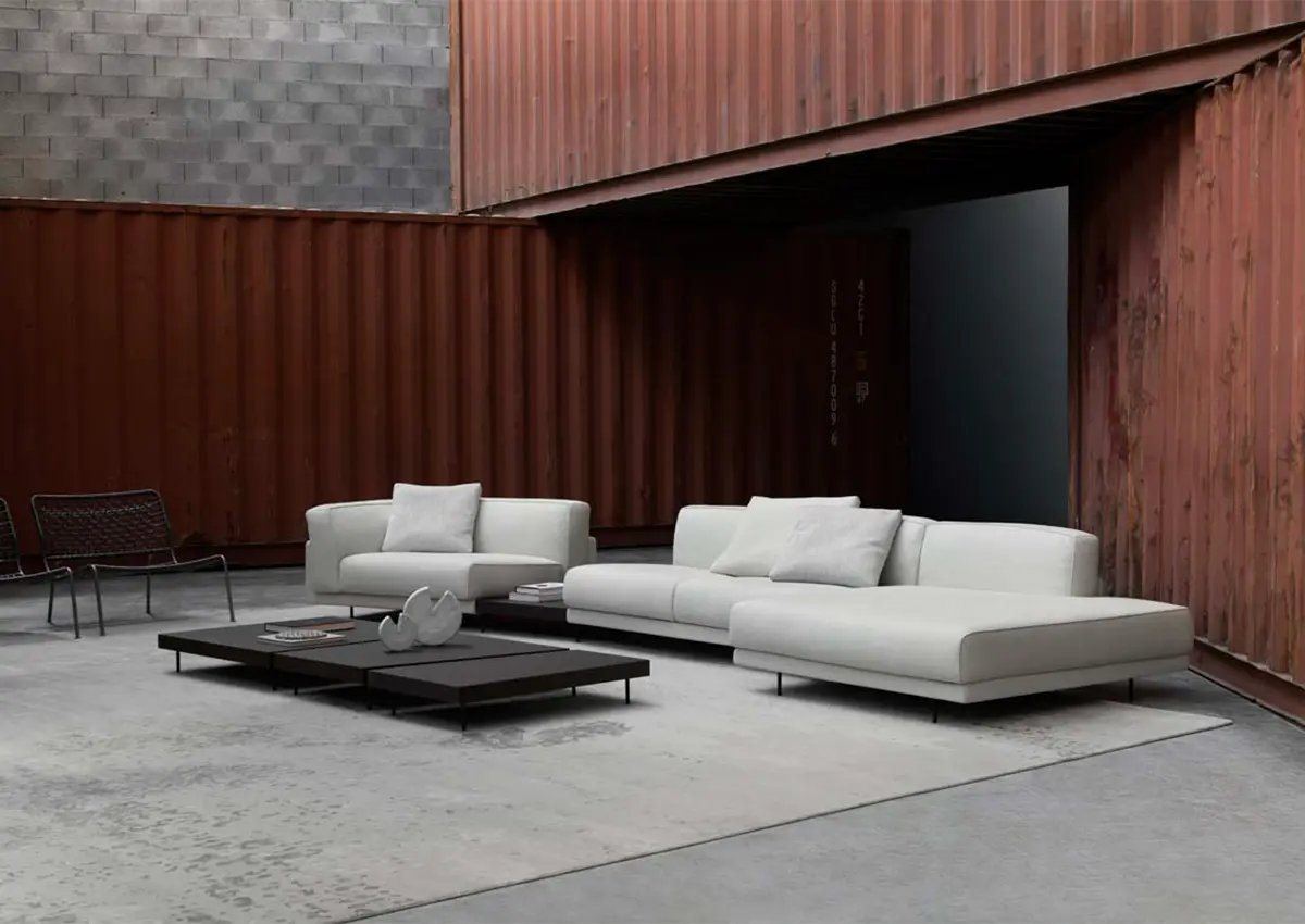 Modularna bela sedežna garnitura Living Divani 2025 v industrijskem prostoru z betonom in kovino.
