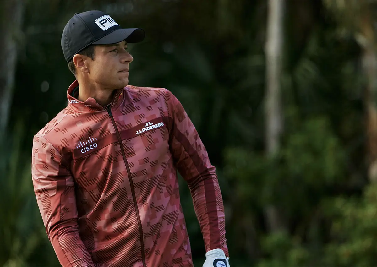 Golfist v rdeči jakni J.Lindeberg med zamahom na igrišču, del kolekcije Augusta Capsule.