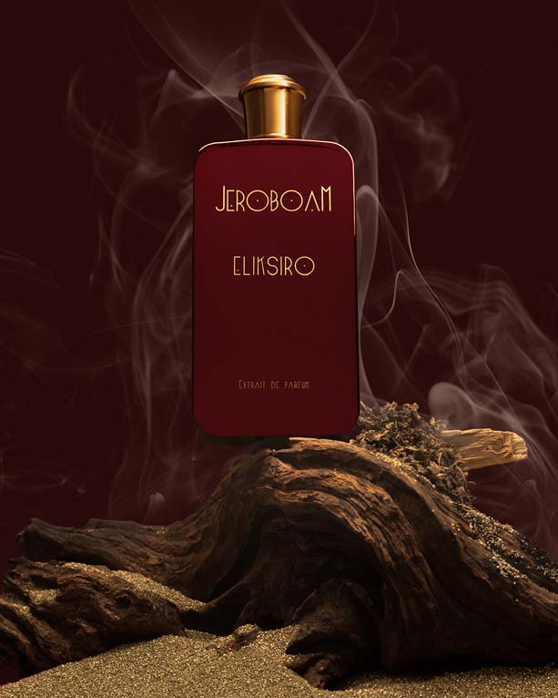 Kampanjski motiv parfuma Jeroboam Eliksiro z lesom, peskom in dimom v bordo ozadju.